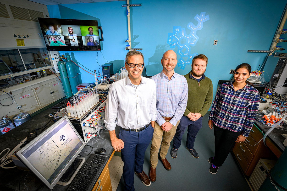 Illinois researchers led an international team that combined powerful AI and a molecule-making machine to find the best conditions for automated complex chemistry. Pictured, from left: University of Illinois chemistry professor Martin D. Burke, materials science and engineering professor Charles M. Schroeder, graduate student Nicholas Angello and postdoctoral researcher Vandana Rathore. Pictured on the screen behind them are international collaborators, led by professors Bartosz A. Grzybowski and Alán Aspuru-Guzik.