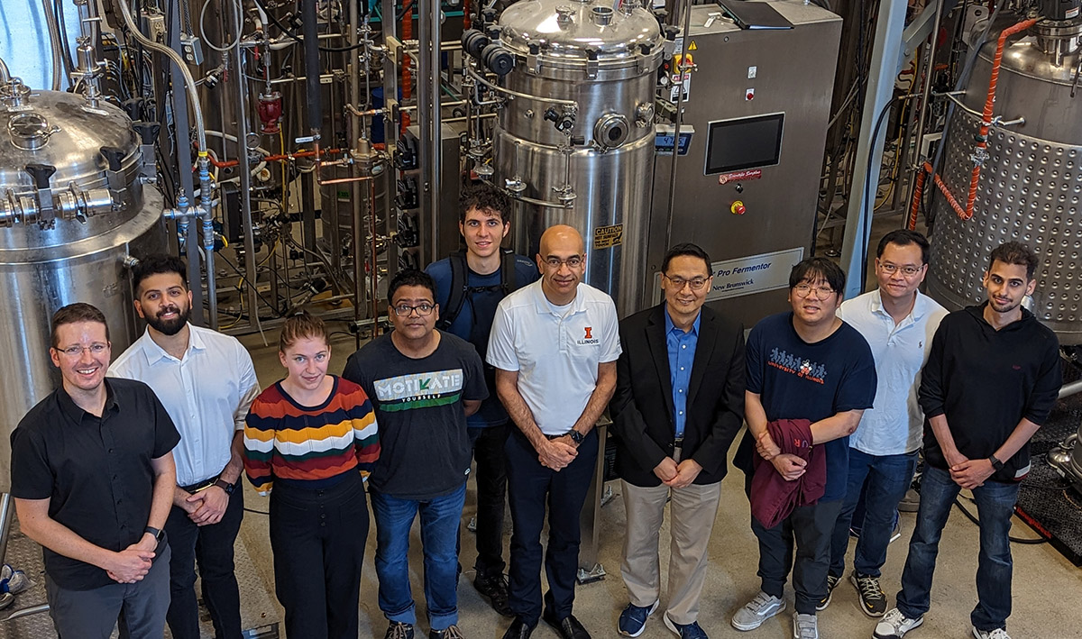 The Illinois research team in front of a fermenter at IBRL, from left: Jeremy Guest, Sarang Bhagwat, Jayne Allen, Somesh Mishra, Benjamin Crosly (back), Vijay Singh, Huimin Zhao, Shih-I Tan, Vinh G. Tran, and Saman Shafaei.