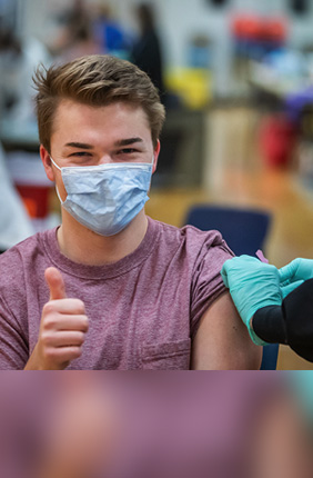 A student who works at a COVID-19 testing center gives a thumbs up after receiving a COVID-19 vaccine. Students may now enroll in a study to help understand the effectiveness of vaccines in reducing the spread of the coronavirus.