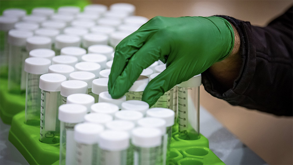 A gloved hand places saliva testing samples in a tray at Illinois