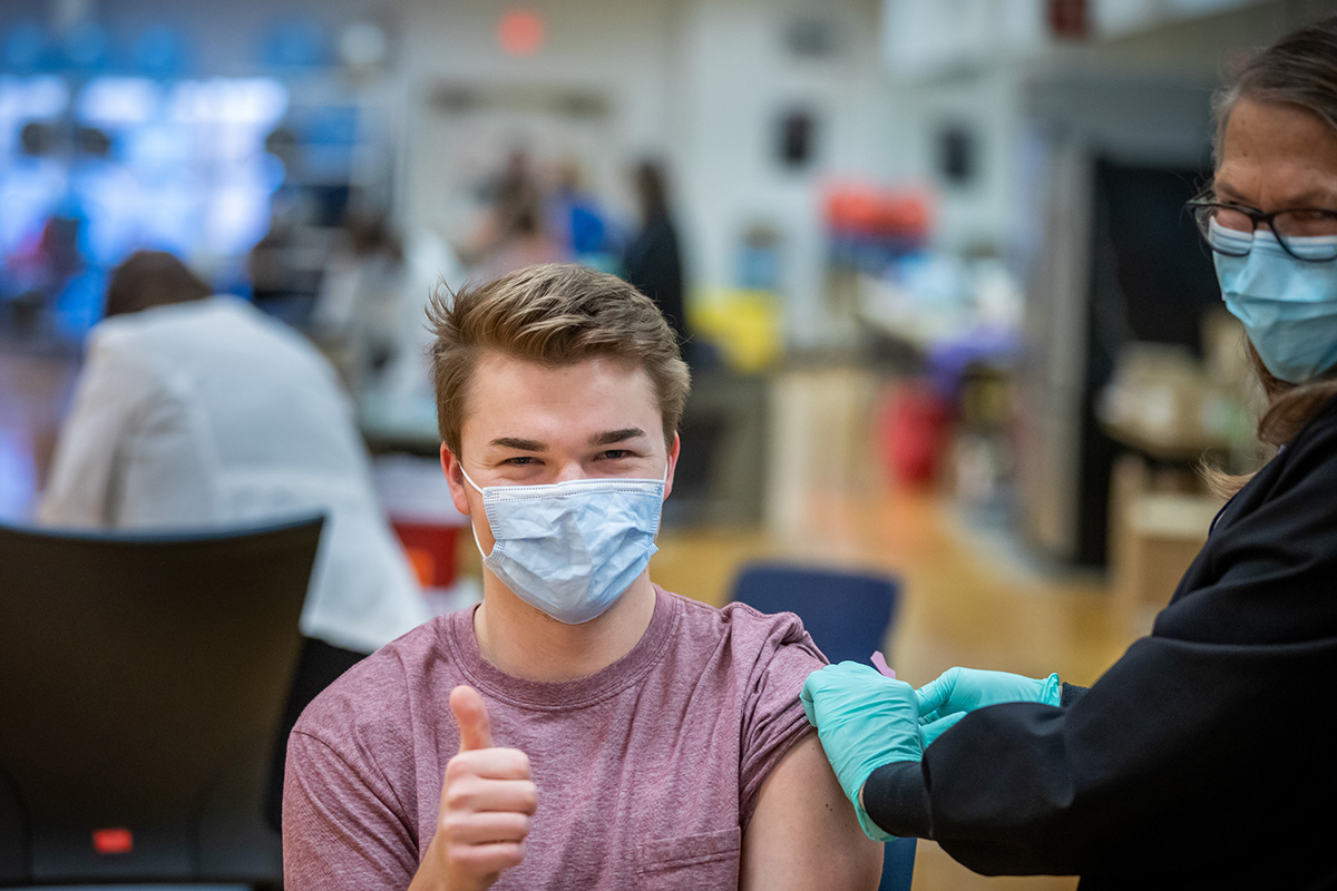 A student who works at a COVID-19 testing center gives a thumbs up after receiving a COVID-19 vaccine. Students may now enroll in a study to help understand the effectiveness of vaccines in reducing the spread of the coronavirus.